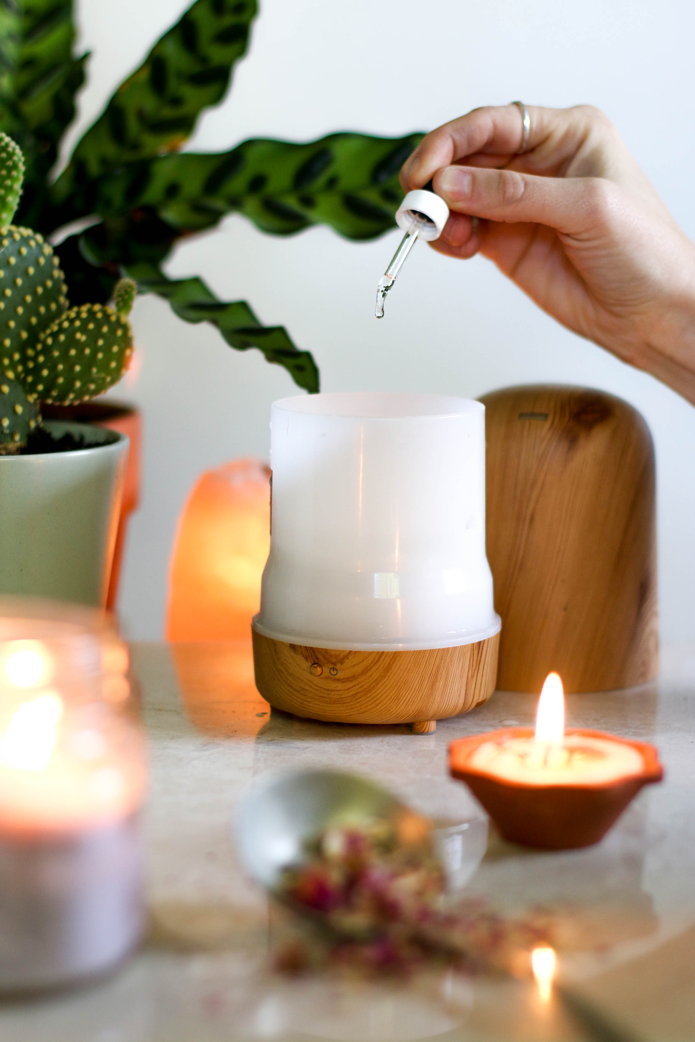 Hand-dropping-oil-into-essential-oil-diffuser-with-candles-and-plants